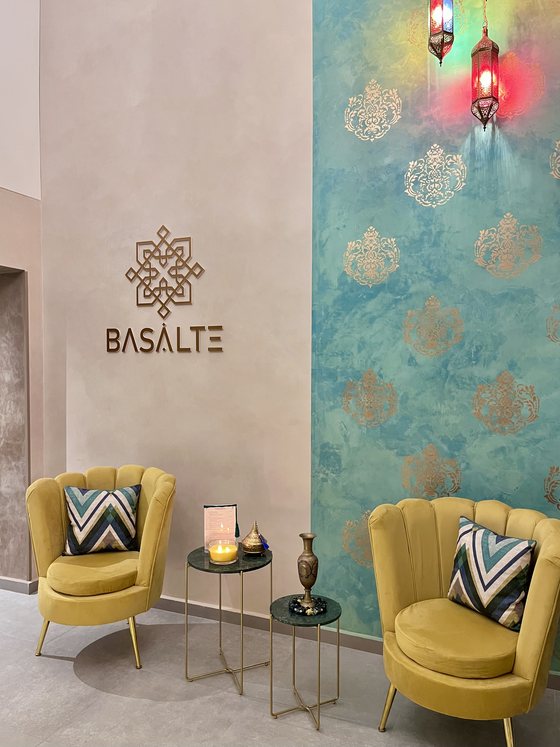 Le salon d'accueil : fauteuils en velours moutarde, tables basses en laiton et bougies devant le mur Basalte